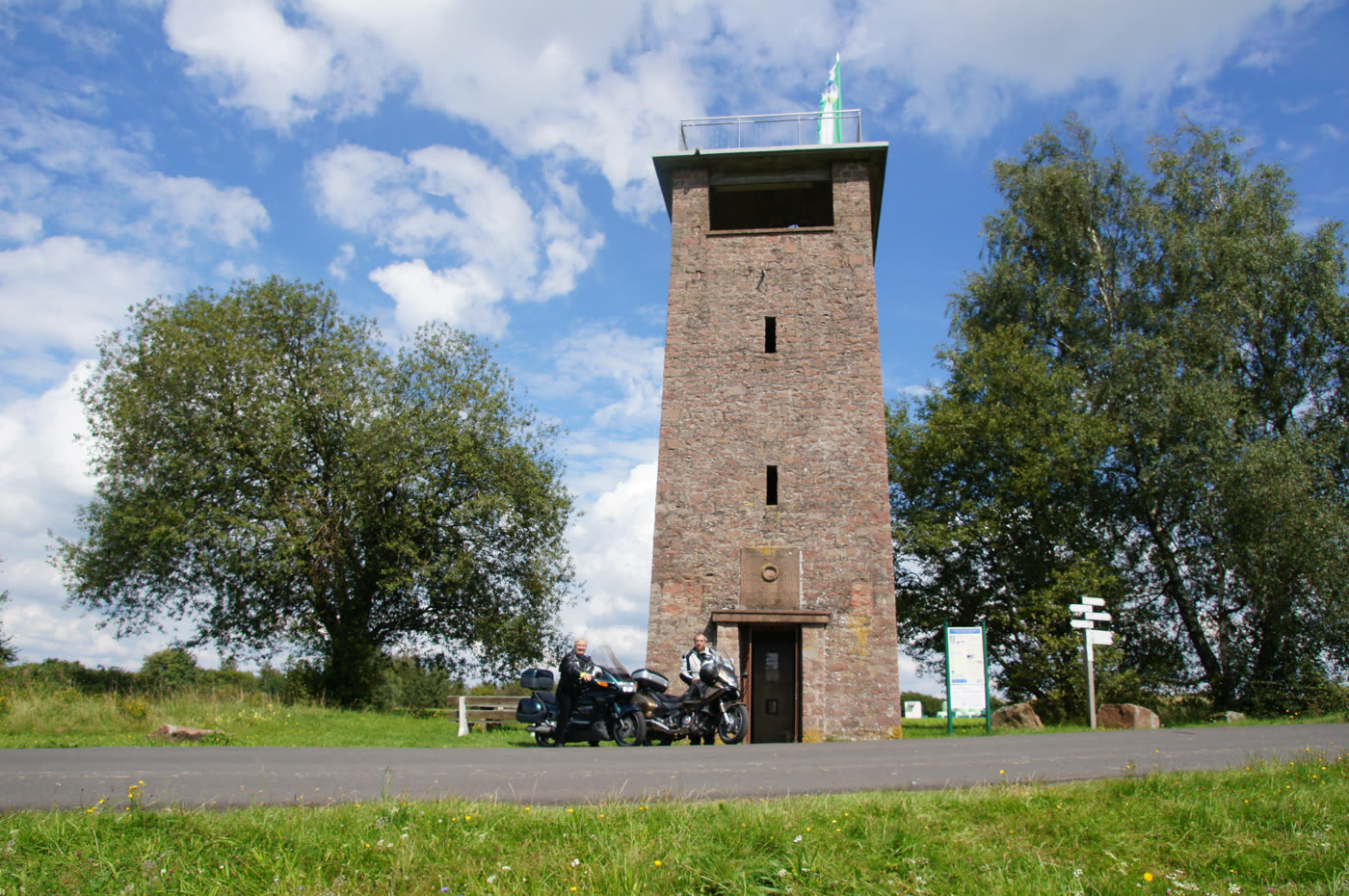 Roter Sandsteinturm auf einer Wiese, davor abgestellte Motorräder Roter Sandsteinturm auf einer Wiese, davor abgestellte Motorräder
